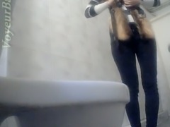 Slender white stranger girl in the toilet room shows her ass on voyeur cam